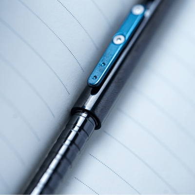 A close-up shot of a black and silver pen with a metallic blue clip, resting diagonally on lined paper.