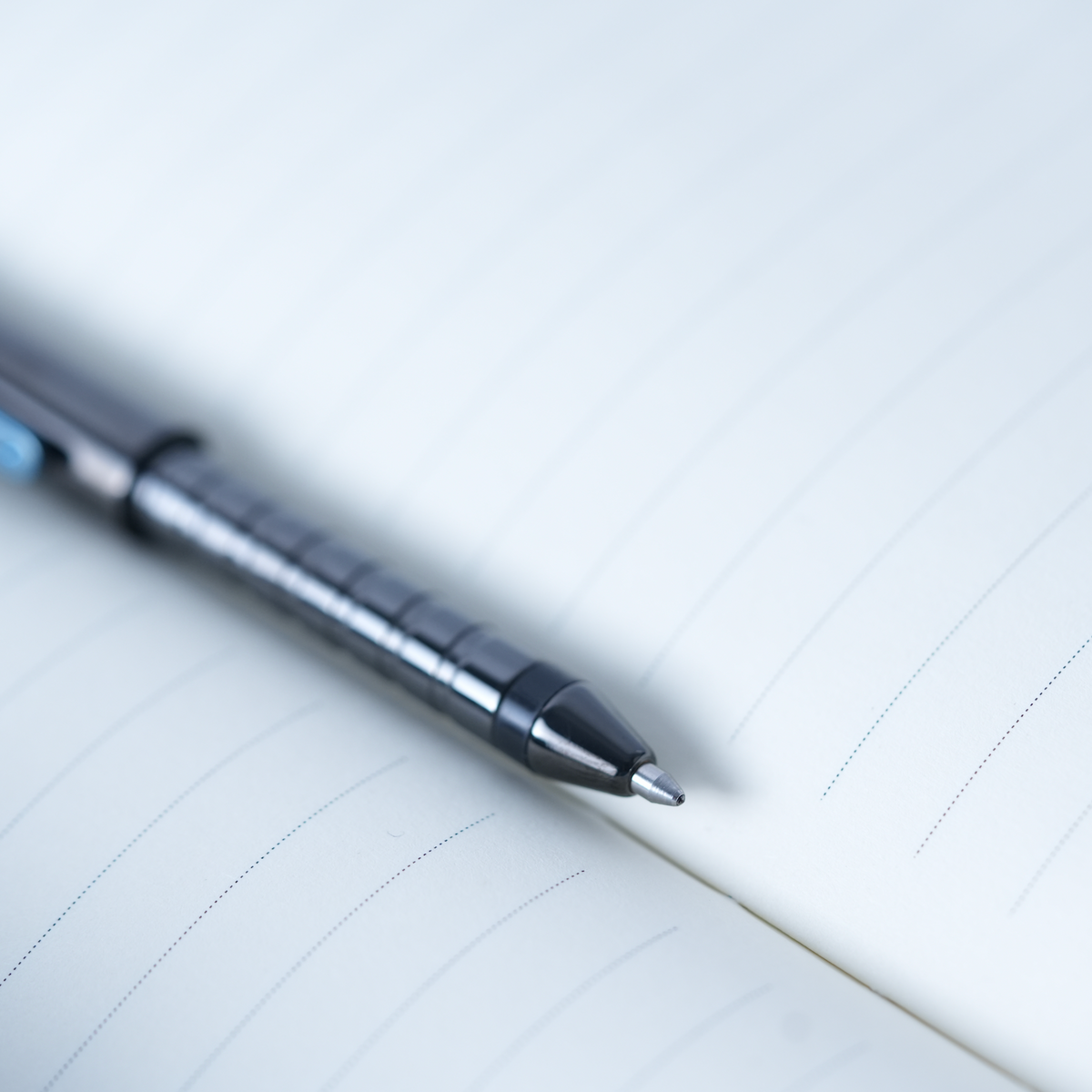 A close-up shot of a sleek black and silver ballpoint pen resting diagonally on the corner of an open lined notebook.
