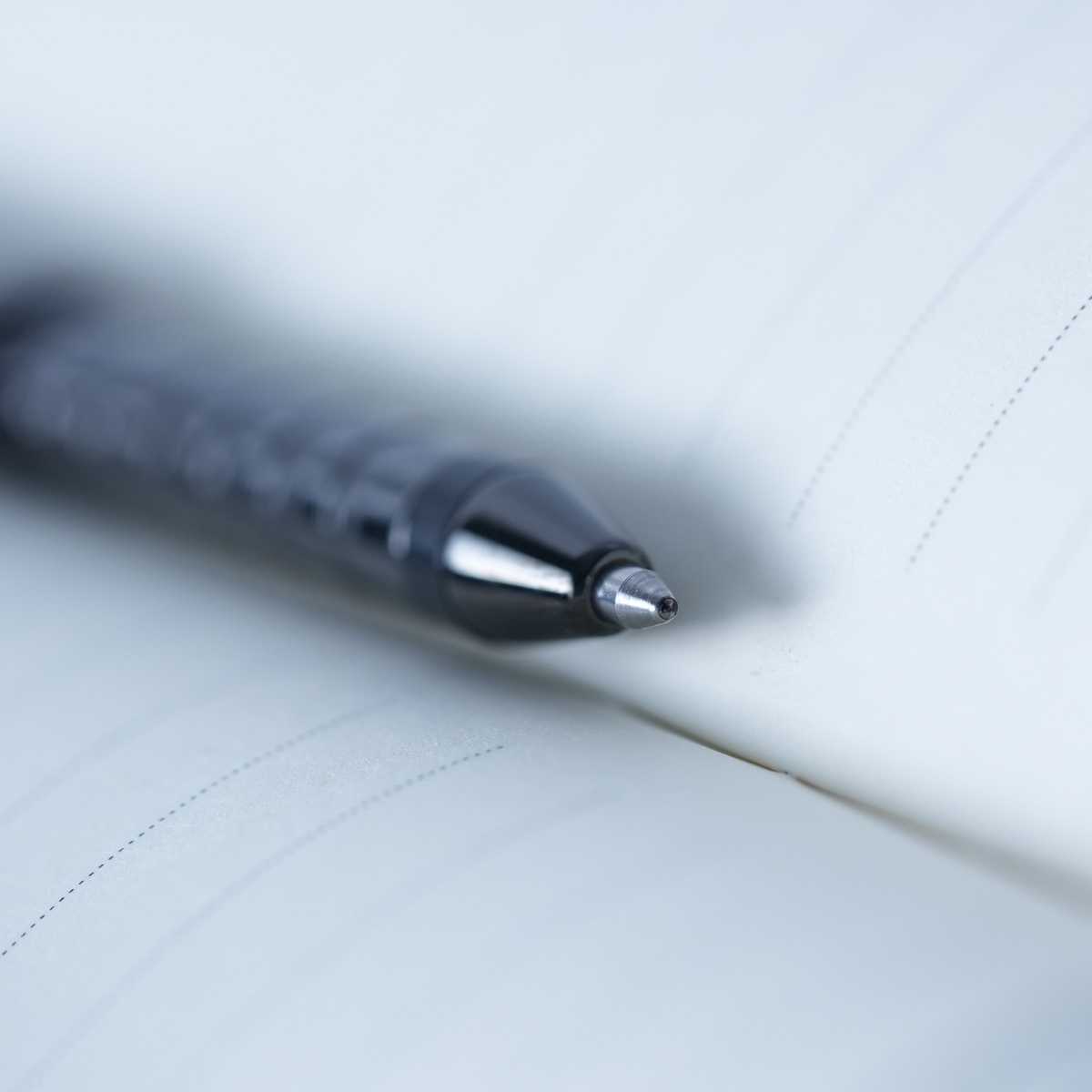 A close-up, shallow depth-of-field shot of a black ballpoint pen resting on the pages of an open lined notebook.