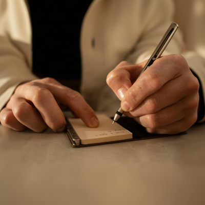 Person writing on a small notepad with a pen.