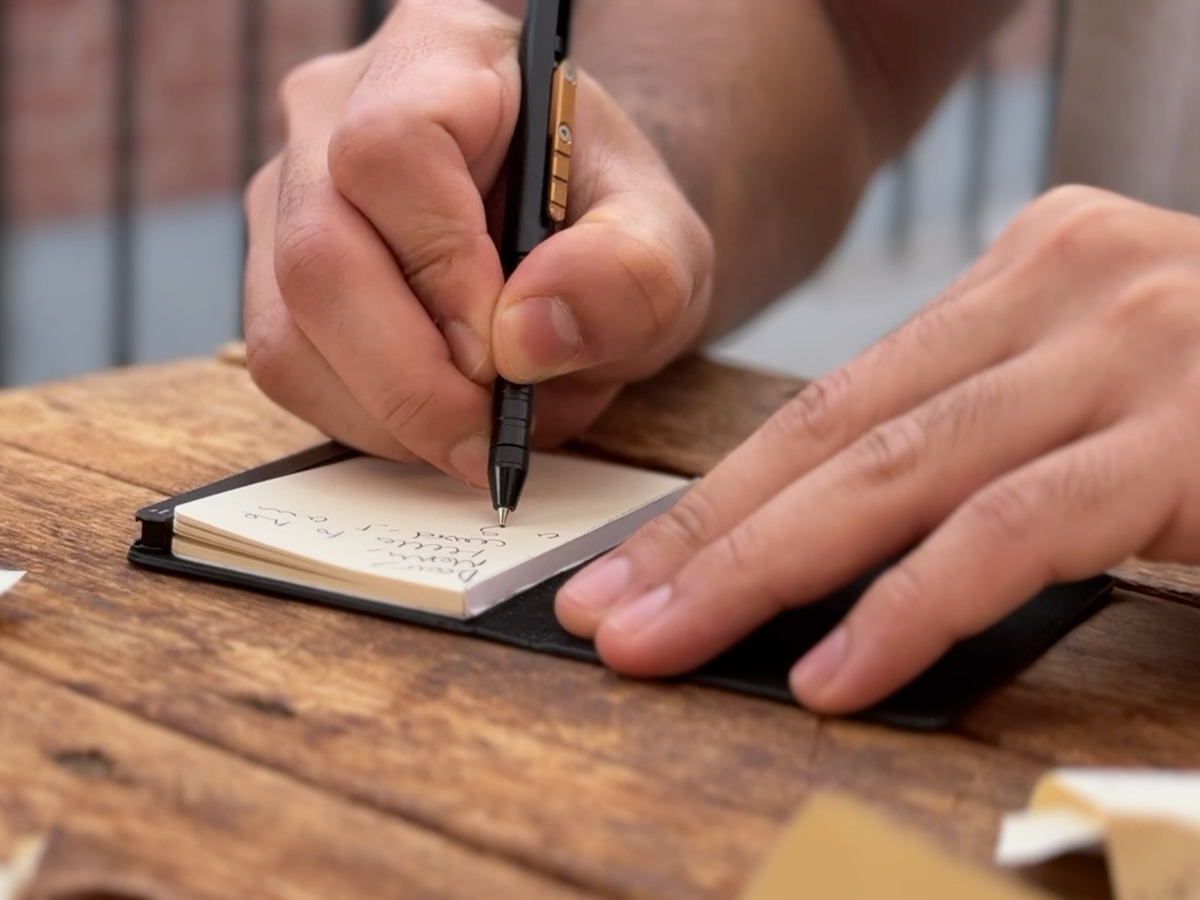 Person writing in a small notebook with a pen on a wooden surface