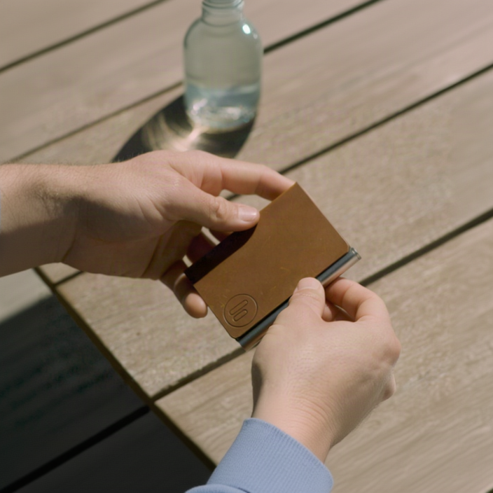 Brown leather wallet being held by a person on a wooden surface