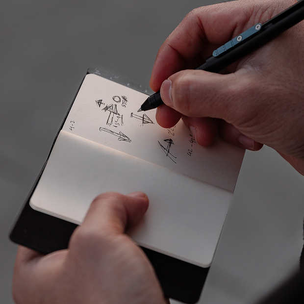 Person drawing on a small notebook with a pen.
